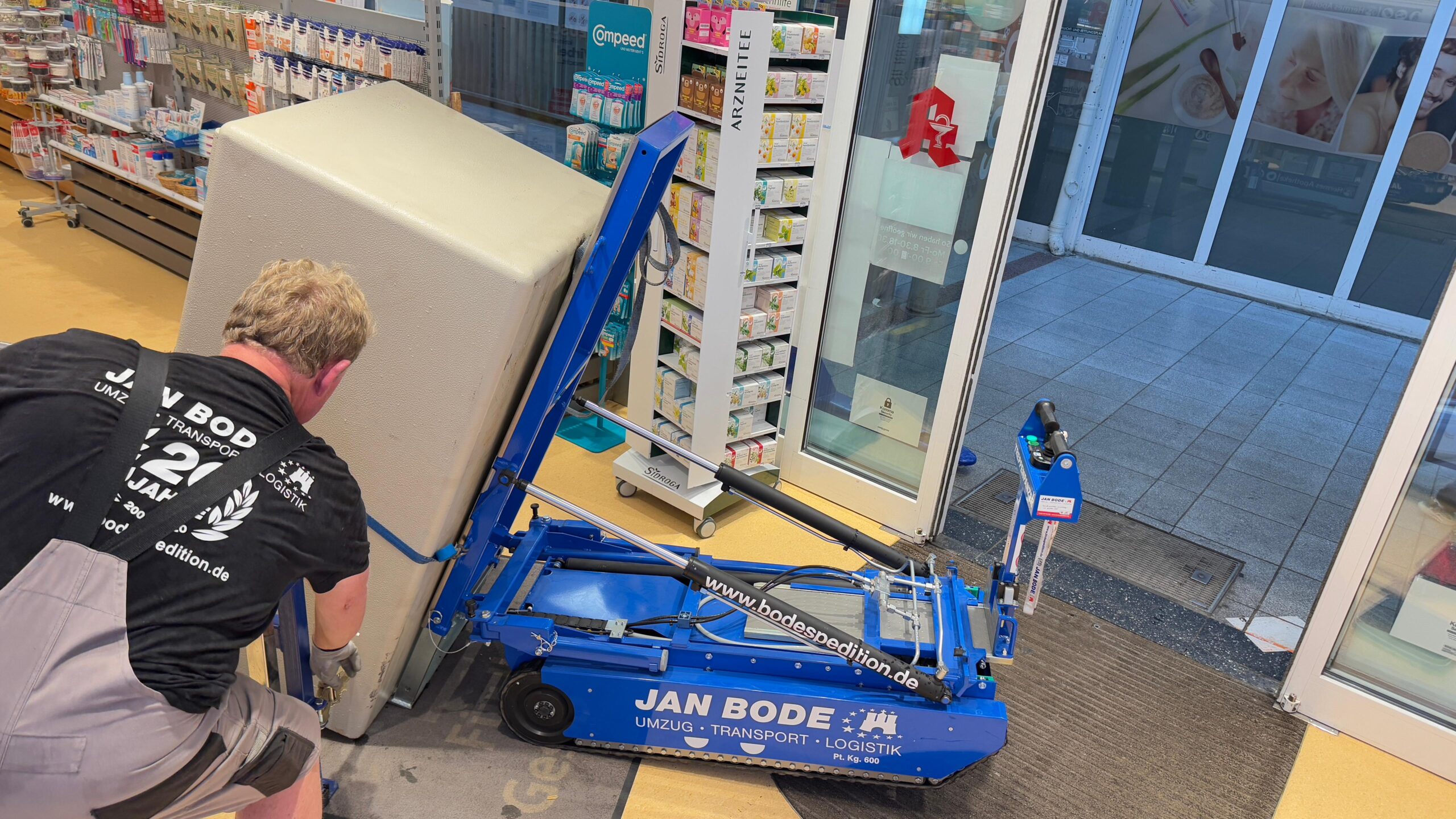 Ein Mann bewegt mit Treppensteiger einen großen Tresor durch eine Ladentür